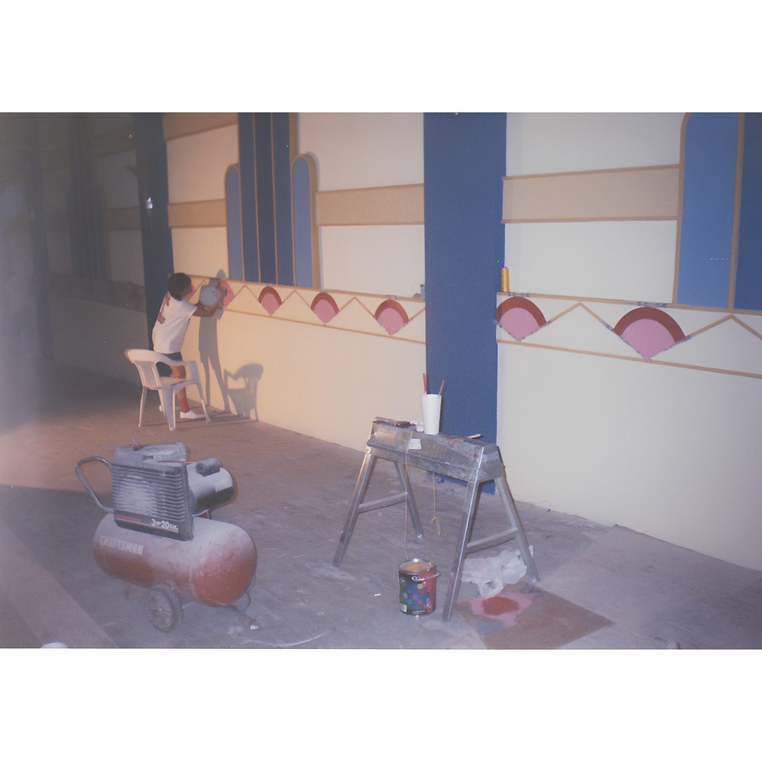 Person painting large geometric mural indoors.