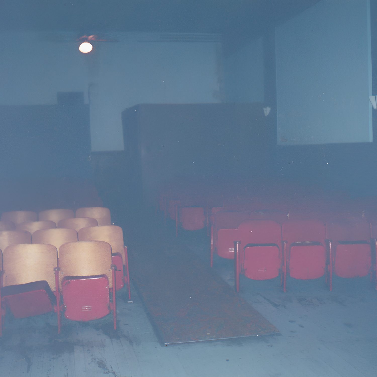 Dimly lit, empty theater with red chairs.